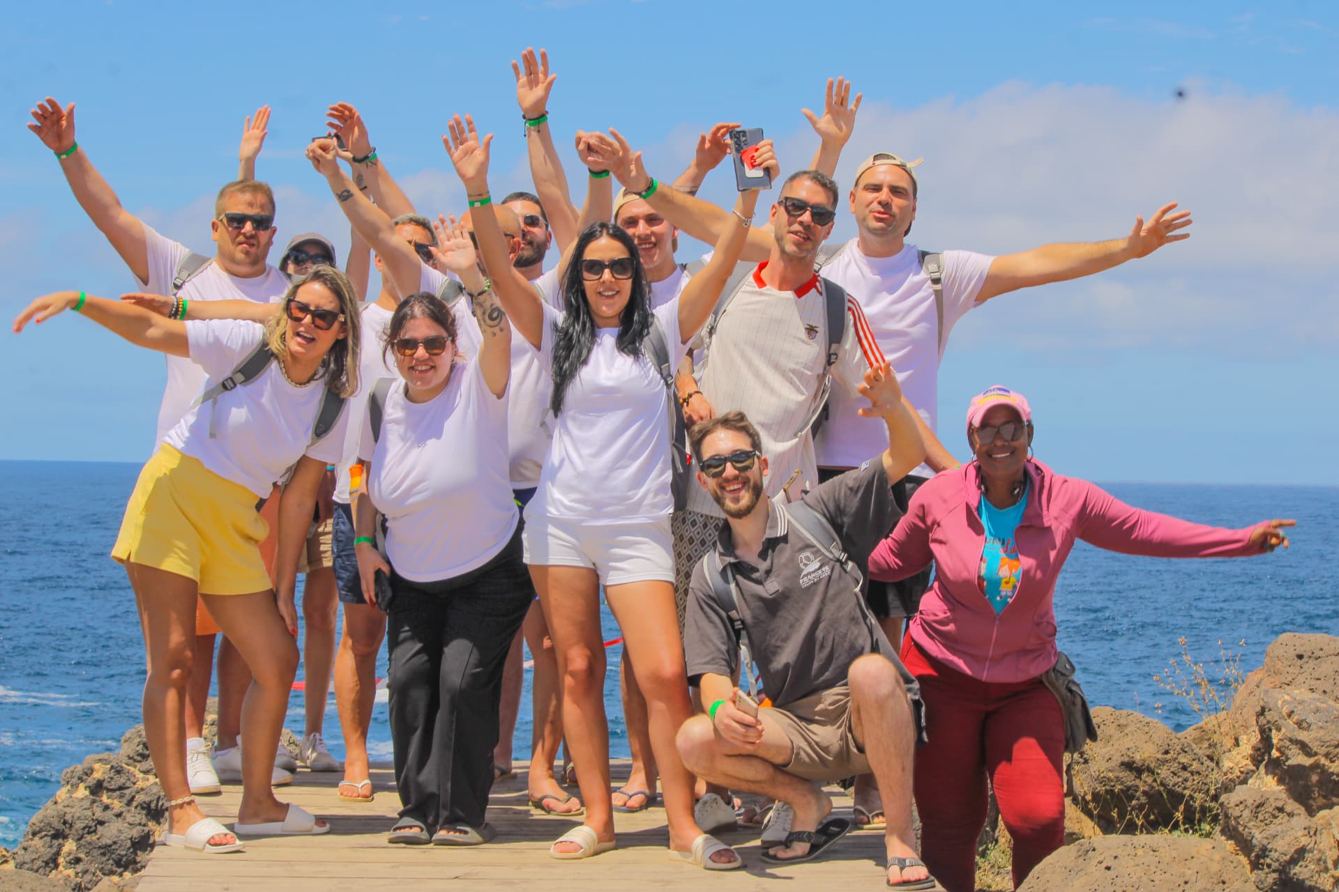 Grupo de visitantes da Krioula Tour de braços no ar num miradouro sobre o mar, Ilha do Sal